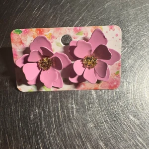 Rosa blomformade örhängen - Superfina örhängen i form av stora rosa blommor med guldiga detaljer i mitten. Blommorna har flera lager av kronblad som ger en 3D-effekt och sticker ut på ett coolt sätt. Perfekt för dig som vill ha något som syns och ger en färgklick till din stil.