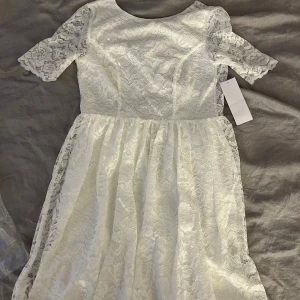 Vit spetsklänning från Bubbleroom - Supersöt vit långklänning från Bubbleroom med spets över hela klänningen och korta ärmar. Modellen har rund halsringning och ett flowigt fall. Öppen i ryggen. Perfekt studentklänning! Helt ny, aldrig använd