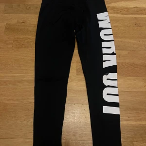Svarta sportleggings från Gina Tricot - Svarta sportleggings från Gina Tricot, modell Filippa p sport leggings. De har en vit WORK OUT-text längs ena benet och dragkedja vid benslutet. Materialet är stretchigt med 91% polyamid och 9% elastan.