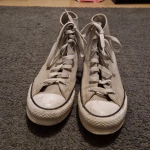 Beige Converse All Star high-tops - Klassiska beige Converse All Star high-top sneakers med vit gummisula och rund tå. Skorna har snörning och den ikoniska loggan på sidan. Tillverkade i canvas med slitstark sula och cool retrostil som funkar till allt.