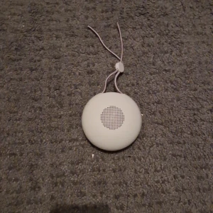 Portabel Mini Bluetooth-högtalare - Smidig och kompakt Bluetooth-högtalare i vitt med praktisk snodd för enkel upphängning. Perfekt för resor eller utomhusbruk. Högtalaren är i gott skick utan synliga repor eller skador. Laddningsbar och enkel att använda med alla Bluetooth-enheter.
