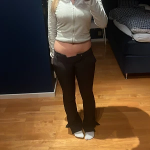 Svarta bootcut kostymbyxor med slits - Snygga svarta kostymbyxor med bootcut passform och slits vid bensluten. Byxorna har låg midja och klassisk rak design med hällor för bälte. Tyvärr har dom blivit för små för mig så de kommer inte till användning.