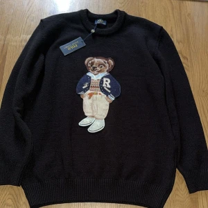 Svart stickad tröja Polo Bear Ralph Lauren - Svart stickad tröja från Polo Ralph Lauren med ikoniska Polo Bear broderad framtill. Rund halsringning, ribbade muddar och långärmad modell. Perfekt statement-piece för dig som gillar klassisk stil med en twist.