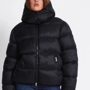 Svart pufferjacka med huva - Säljer en svart pufferjacka med stor, mysig huva och dragkedja .Perfekt för kalla dagar när du vill hålla värmen.