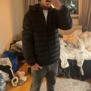 Svart pufferjacka från Stone Island - Pris kan diskuteras!Säljer en svart pufferjacka från Stone Island med ikonisk patch på ärmen. Jackan har huva, dragkedja framtill och quiltad design som ger en schysst look. Perfekt för kalla dagar och riktigt snygg till jeans eller cargo. Jackan är i medium och har en clean, modern vibe.