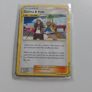 Guzma & Hala Tag Team - Cool Pokémon Trainer-kort med Guzma & Hala från TAG TEAM-serien! Perfekt för dig som vill boosta din samling eller ta ditt spel till nästa nivå. Kortet är illustrerat av Ken Sugimori och är ett måste för alla Pokémon-fans.