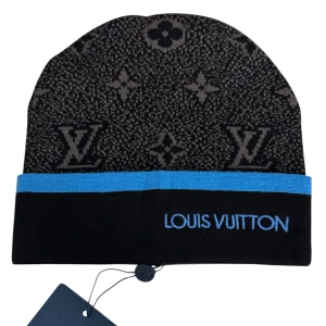 Louis Vuitton svart och blå mössa - Snygg svart mössa från Louis Vuitton med klassiskt monogrammönster i grått och en blå kant. Broderad Louis Vuitton-logga framtill. Tillverkad i mjukt stickat material som håller dig varm och stilsäker under kalla dagar.