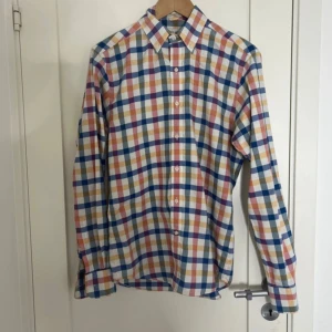 Rutig skjorta från John Henric - Färgglad rutig skjorta från John Henric med klassisk krage och knappar framtill. Skjortan har lång ärm och är gjord i mjuk bomull som är lätt att stryka. Färgerna är blå, rosa, orange, vit, vilket ger en riktigt fräsch vibe.