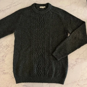 Mörkgrå stickad tröja Kappahl S - Mysig mörkgrå stickad tröja från Kappahl i storlek S. Tröjan har ett snyggt flätmönster framtill och ribbade muddar vid hals, ärmslut och nederkant. Perfekt för kyliga dagar och passar dig som gillar klassisk stil.