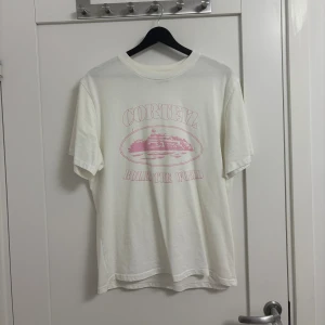 💗 Corteiz T-Shirt “Rules The World” (Pink Print) – Storlek M - Vit Corteiz-t-shirt med rosa grafiskt tryck fram.  Storlek: M Skick: Mycket bra