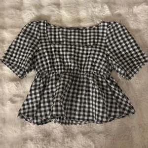 Rutig blus med puffärm från Shein - Supersöt svartvit rutig blus från Shein med fyrkantig ringning och korta puffärmar. Modellen har en lätt volang nedtill och markerad midja för en feminin siluett. Perfekt för dig som gillar trendiga och lekfulla toppar.