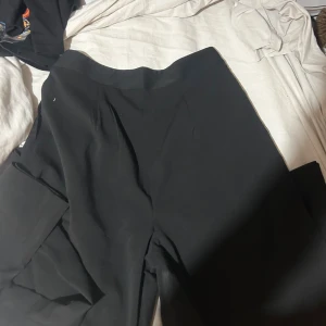 Svarta kostymbyxor från Shein M - Snygga svarta kostymbyxor från Shein i storlek M. Byxorna har en rak och lite loose passform med hög midja och stilrena pressveck framtill. Materialet är mjukt och lätt, perfekt för en clean och modern look.