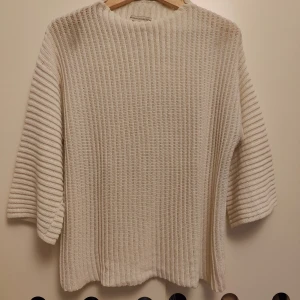 Ribbad beige stickad tröja - Ribbad stickad tröja i beige från Mudo Collection. Tröjan har en loose passform med trekvartsärm och rund hals. Materialet är mjukt och grovstickat, perfekt för lager på lager. Enkel och clean design som funkar till jeans eller kjol.