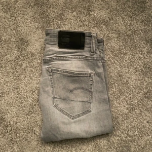 G-star raw jeans slim fit - Snygga ljusgrå jeans från G-star raw med klassisk femficksdesign och diskret Gstar-logga på bakfickan. Jeansen har ett smalt snitt och är tillverkade i mjukt jeanstyg med stretch.  Ett litet hål på knät men går att laga väldigt enkelt och billigt. Otroligt lika dondups i deignen. W29 L30