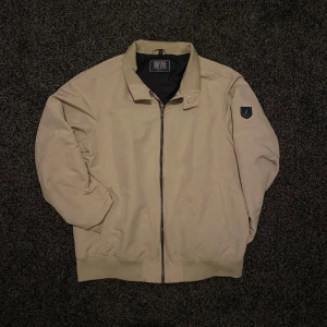 Beige bomberjacka från Jofama - Snygg beige bomberjacka från Jofama med svart foder och ribbade muddar. Perfekt för dig som gillar stilren och enkel design med praktiska fickor både på insidan och utsidan.    Den är i stl M och nypris ligger på ca 1900kr