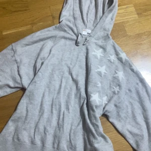 Grå hoodie med vita stjärnor Gina Tricot - Snygg grå hoodie från Gina Tricot i storlek 158/164. Tröjan har huva med snörning och är dekorerad med vita stjärnor på framsidan och ärmen. Mjuk bomullskänsla och långärmad modell, perfekt för chill dagar.