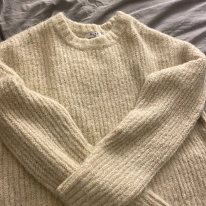 Beige stickad tröja från NA-KD - Mysig beige stickad tröja från NA-KD med grov ribbad struktur. Tröjan har rund halsringning och långa ärmar med breda muddar. Perfekt för lager-på-lager och chill dagar.