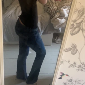 Blå bootcut jeans låg midja - Snygga blå jeans med bootcut och låg midja. Jeansen har klassisk femficksdesign, dragkedja och knapp framtill. Materialet är jeans med lätt tvättade detaljer för en cool look. Passar dig som gillar avslappnad stil med lite retrovibe.Ett superlitet hål på ena knät och ett ”bält band” som låssnat nere men annars inga syndliga täcken på användning.