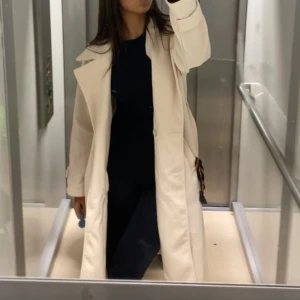 Beige trenchcoat med stora slag - Snygg beige trenchcoat med stora slag och klassisk krage. Jackan har långa ärmar med knappdetaljer vid mudden och två fickor framtill. Stilren och enkel design som ger en clean look. Perfekt för dig som gillar minimalistiskt och tidlöst.
