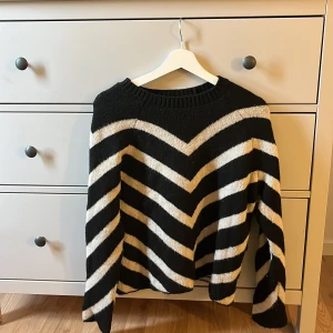Svartvit stickad tröja från ONLY - Säljer en stickad tröja från ONLY i storlek S med svart och vit zigzag-randigt mönster. Tröjan har rund hals och långa ärmar, perfekt för dig som gillar grafiska mönster och vill ha en mysig look. Passar dig som vill sticka ut lite extra.