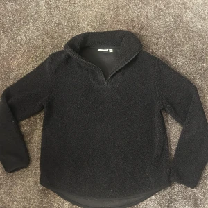 Svart fleece-tröja från Kappahl - Mysig svart fleece-tröja från Kappahl i storlek XS. Tröjan har lång ärm, hög krage och en praktisk half zip-dragkedja framtill. Perfekt när du vill hålla dig varm och ändå se chill ut. Materialet är mjukt och fluffigt, vilket gör den extra skön att bära.