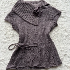 *INTRESSEKOLL** - Unik lila/ brun aktig stickad topp med bred ribbad krage och dekorativ blomrosett. Kortärmad modell med snörning i midjan och snyggt hålmönster nedtill. Perfekt för dig som gillar detaljer och vill ha något annorlunda i garderoben.