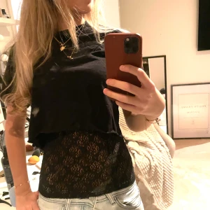 Svart spetsig linnetopp - Säljer en svart, tight linnetopp i spets med snyggt mönster. Toppen är ärmlös och har en smickrande passform som sitter nära kroppen. Perfekt att styla under en croppad t-shirt eller för sig själv. Spetsen ger en cool och feminin vibe.