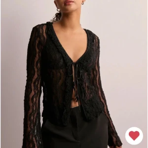 Svart spetsblus med snörning från Pieces - Säljer en svart transparent spetsblus från Pieces i storlek XS. Blusen har långärmade ärmar, v-ringad hals och snygg snörning framtill. Spetsen har ett vågigt mönster som ger en extra cool vibe. Perfekt för dig som gillar detaljer och vill sticka ut. Aldrig använd! 