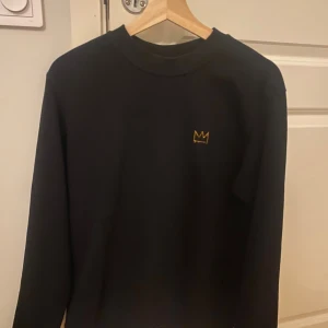 Svart sweatshirt med guldig hov1 kron - Priset kan diskuteras!! Svart sweatshirt med en hov1 krona på bröstet. Perfekt för dig som gillar hov1. Mjuk insida och klassisk passform. Säljer pågrund av att den tyvärr inte kommer till användning. 