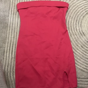 Röd axelbandslös kortklänning Wellsoft - Säljer en snygg rosa axelbandslös kortklänning från Wellsoft. Klänningen har en tight passform, liten slits framtill och dragkedja bak. Perfekt för dig som vill sticka ut med en enkel men stilren look.