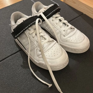 Adidas Forum Low Parley sneakers vita - Säljer ett par Adidas Forum Low Parley sneakers i vitt med svarta detaljer och klassiska tre ränder på sidan. Skorna har snörning, rund tå och är tillverkade i syntetmaterial med skinnkänsla. Adidas-logga på hälen och svart rem med texten 'For the Oceans'. Original pris 1100-1400kr