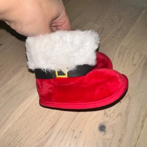 Röda tomteboots för baby tomte skor jul skor 🎄jul tofflor  - Supergulliga röda tomteboots för baby med vit fluffig kant och svart bälte med gul spänne. Sulan har halkskydd med snöflingor. Perfekta för julens mysiga stunder och foton. Mjukt material som känns skönt mot små fötter.