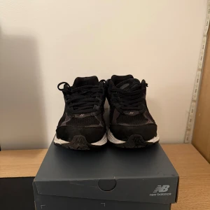 Svarta New Balance 2002R sneakers - Säljer ett par svarta New Balance 2002R sneakers med vit sula. Skorna har mesh och mockadetaljer, klassisk N-logga på sidan och snörning. Perfekta för dig som gillar stilrena och bekväma sneakers med sportig vibe.