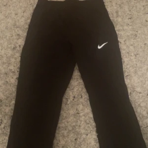 Svarta Nike Dri-FIT träningsbyxor - Svarta träningsbyxor från Nike med Dri-FIT-teknologi som transporterar bort fukt. Byxorna har en smal passform och klassisk Nike-logga på låret. Perfekta för dig som gillar sportig stil och vill ha bekväma byxor till träning. Passar som XS