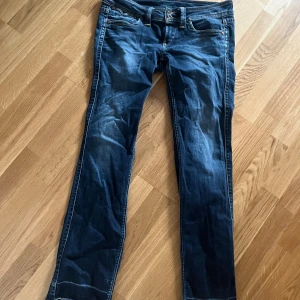 Blå jeans från Pepe Jeans, lowwaist - Säljer ett par klassiska blå jeans från Pepe Jeans med snygga slitningar och kontrastsömmar. Modellen har bootcut nedtill och normal passform, med broderad logga på bakfickan. Tillverkade i bomull med lite stretch för extra komfort.