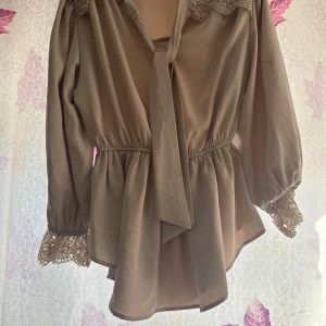 Beige blus med spets och knyt - Säljer en beige blus med vackra spetsdetaljer vid axlar och ärmslut. Blusen har knytband i halsen, markerad midja och trekvartsärmar med volang. Perfekt för dig som gillar romantisk och feminin stil.