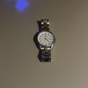 Silverfärgad klocka från black oak - Stilren klocka från Urban Park med rund vit urtavla och datumvisning. Armbandet är i blankt silverfärgat metall och har klassisk länkdesign. Klockan har minimalistiska markeringar och en snygg, modern look som passar till många stilar.