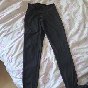 Svarta höga sport leggings i stretchigt material - Svarta sport leggings med hög midja i ett stretchigt och mjukt syntetmaterial. Perfekta för träning eller chill, med bred linning och figurnära passform. Snygga och enkla att matcha med allt.