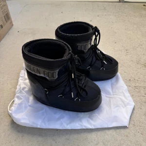 Moon Boots - svarta med snörning - Säljer ett par svarta Moon Boots med klassisk logga runt skaftet. Skorna har snörning framtill och är tillverkade i syntetmaterial med vadderad insida för extra värme. Perfekta för vintern och riktigt snygga till vinterlooken. Dem är använda från och till under en vinter säsong, så inte utslitna. Det finns ett rött litet skrapmärke på insidan av ena skon, annars helt felfria! Skrapmärket kan säkerligen målas över av svart tushpenna! Nypris 2285kr.