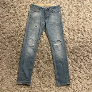 Ljusblå slitna jeans från Jack & Jones - Ljusblå jeans från Jack & Jones med slitningar. Hål vid gylfen därför neddraget pris. Slim fit passform