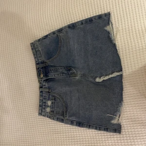 Blå jeanskjol med slitna detaljer - Snygg blå jeanskjol i kort modell med råa, fransiga kanter och slitna detaljer både fram och bak. Klassisk femficksdesign och bälteshällor. Perfekt för dig som gillar en avslappnad och trendig stil. Från shein, köpte för: 200kr? 