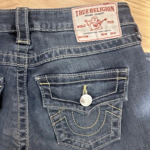 True Religion Joey Low Rise Flare Jeans - Snygga blå jeans från True Religion, modell Joey Low Rise Flare. De har låg midja, utsvängda ben och coola detaljer, storlek 25