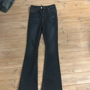 Mörkblå bootcut jeans från NLY - Snygga mörkblå jeans från NLY med bootcut passform och klassiska kontrastsömmar. Jeansen har fem fickor, hällor för bälte och en läderpatch bak i midjan. Perfekta för dig som gillar en retrovibe och vill ha ett par jeans med lite utsvängda ben.
