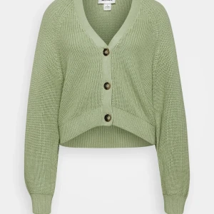 Grön stickad kofta från Monki - Snygg ljusgrön stickad kofta från Monki med v-ringning och stora knappar framtill. Modellen är croppad med långa ärmar och ribbade muddar. Perfekt att slänga över en t-shirt för en chill look.