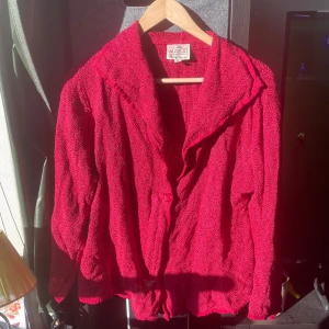 Röd kofta från Masai Clothing Company - Säljer en röd kofta från Masai Clothing Company i storlek M. Koftan har en lös passform, lång ärm och är tillverkad i ett strukturerat tyg med krage och knappar framtill. Perfekt för dig som gillar färg och en chill vibe.