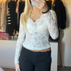 Vit spetsblus med blommönster - Säljer en vit, långärmad blus i spets med blommigt mönster och v-ringad hals. Blusen är genomskinlig och har en feminin, figurnära passform som ger en snygg siluett. Perfekt för dig som gillar romantiska detaljer och vill sticka ut. Aldrig använd 