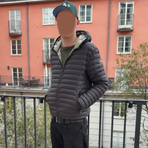 Svart dunjacka med huva från Colmar  - Säljer en svart dunjacka från Colmar huva och snygga horisontella sömmar. Jackan har dragkedja framtill, två sidofickor med dragkedja och en diskret logga på ärmen. Perfekt för kyliga dagar och har en modern, clean look.