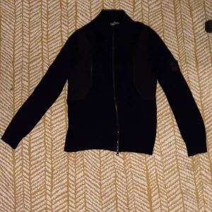 Svart/marinblå kofta från Stone Island (Shadow project)  - Säljer en svart/marinblå kofta från Stone Island med hel dragkedja framtill och ribbade muddar. Medium men passar även Small. Tröjan har lång ärm och klassisk shadow Stone Island-patch på ärmen. Materialet är stickat och känns sitter riktigt bra. Perfekt för dig som gillar stilrena och exklusiva plagg.