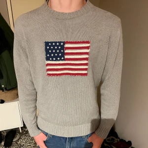 Grå stickad tröja GANT med USA-flagga - Säljer en grå stickad tröja från GANT i 100% bomull. Tröjan har en stor amerikansk flagga broderad på bröstet och ribbade muddar vid hals, ärmslut och nederkant. Perfekt för dig som gillar klassisk och stilren design med en cool detalj. Storlek L men passar M som du ser. Tröjan är knappt använd. Inga defekter eller sådant. 