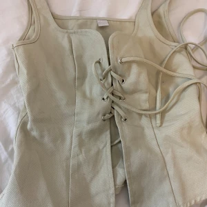 Beige korsett-topp med snörning från Musera - Säljer en beige korsett-topp från Musera i storlek XS. Toppen har breda axelband och snygg snörning framtill som ger en cool vibe. Materialet är kraftigt och känns som bomull, perfekt för att styla med jeans eller kjol.  Säljer för har ingen användning för den 